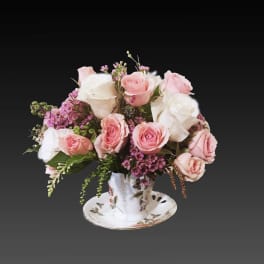 Pink and white roses arranged in a teacup on a saucer