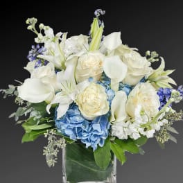 White roses, lilies, and blue hydrangeas in a clear glass vase
