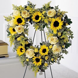 Heart-shaped floral wreath with sunflowers and cream roses on a stand