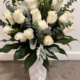 White roses arranged in a tall white vase with silver-green foliage