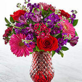 Mixed bouquet of red, pink, and purple flowers in a glass vase