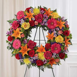 Circular floral wreath on a stand with roses, lilies, gerbera daisies, and small filler flowers