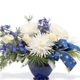 White and blue floral arrangement in a blue vase with a starry ribbon