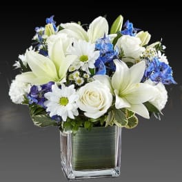 White lilies and roses in a square glass vase with blue flowers