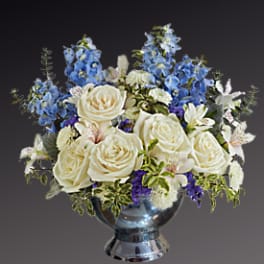 White roses and blue flowers arranged in a silver vase
