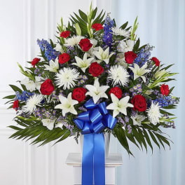 Large standing floral spray with red roses, white lilies, and blue flowers