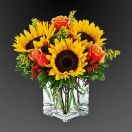 Sunflowers and orange roses arranged in a clear square vase