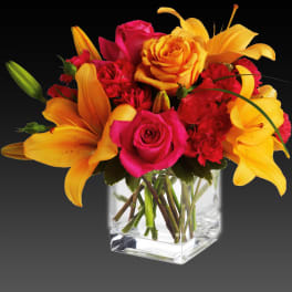 Bouquet of yellow lilies, pink roses, and red carnations in a clear glass vase
