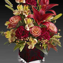 Mixed bouquet with red lilies, pink roses, and burgundy flowers in a glass vase