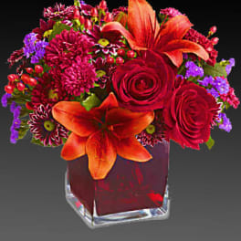 Red and orange floral arrangement in a clear square vase