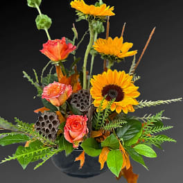 Arrangement of orange roses and yellow sunflowers in a dark vase