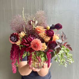Mixed bouquet in a clear glass vase with peach, burgundy, and pink blooms