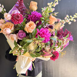 Hand-tied bouquet of peach and magenta flowers wrapped in paper