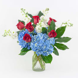 Red roses and blue hydrangeas in a clear glass vase