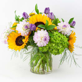 Sunflowers and purple blooms in a clear glass vase