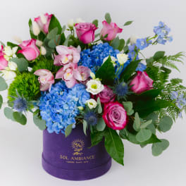 Mixed bouquet in a purple hat box with pink, blue, and white flowers