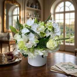 White and pale green floral arrangement in a white container on a table