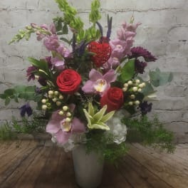 Mixed floral arrangement in a gray vase with red roses and pink orchids