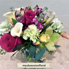 Bouquet of magenta roses, white calla lilies, and purple flowers in a glass vase
