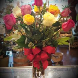 Bouquet of multicolored roses in a clear glass vase with a red bow
