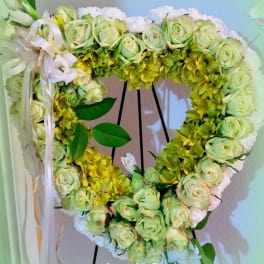Heart-shaped floral wreath with pale green roses and yellow flowers on a stand