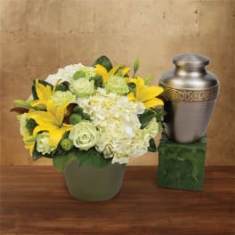 Yellow lilies and white roses arranged beside a silver urn.
