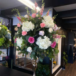 Large pink and white floral arrangement in a tall gold vase