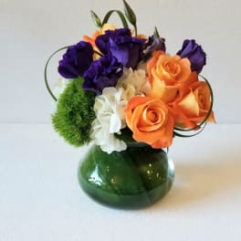 Bouquet of orange roses and purple lisianthus in a green glass vase