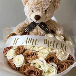Teddy bear atop a bouquet of cream and brown roses with a ribbon
