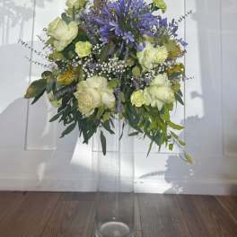 Tall mixed flower arrangement in a clear glass vase with purple and pale green blooms