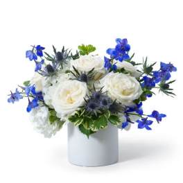 Low white and blue flower arrangement with roses in a white cylinder vase