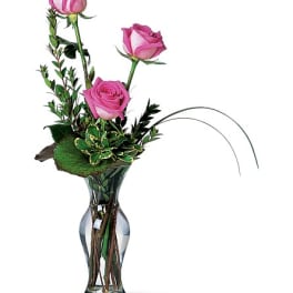 Three pink roses in a clear glass vase with greenery