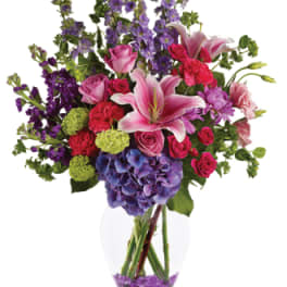 Mixed bouquet of pink roses, lilies, and purple flowers in a glass vase