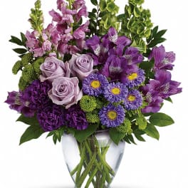 Purple and lavender flowers arranged in a clear glass vase