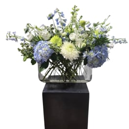 Blue and white floral arrangement in a clear rectangular vase on a black pedestal