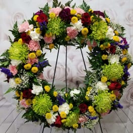 Large floral wreath on a stand with red, pink, white, and yellow blooms