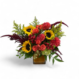 Mixed bouquet with sunflowers, coral roses, and red blooms in a glass vase