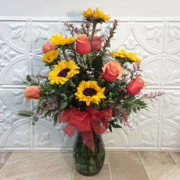 Sunflowers and peach roses in a glass vase with a red bow