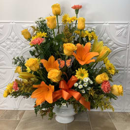 Yellow and orange floral arrangement in a white vase with a ribbon