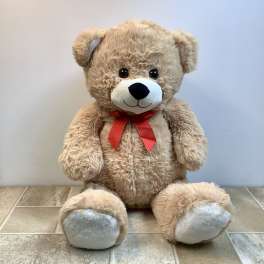 Large tan teddy bear with a red ribbon bow sitting on a tiled floor against a light wall