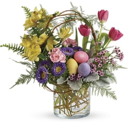 Colorful spring bouquet with tulips, daisies, and decorated eggs in a glass vase