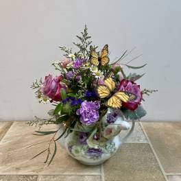 Pink and purple flowers arranged in a floral teapot with butterfly picks