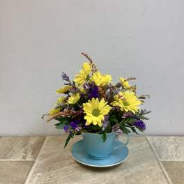 Yellow and purple flowers arranged in a blue teacup with saucer
