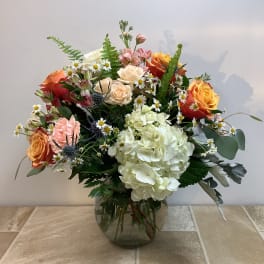 Mixed bouquet of roses, hydrangea, and daisies in a glass vase