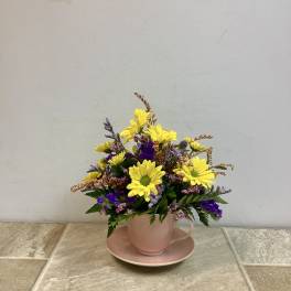 Yellow daisy bouquet in a pink teacup and saucer