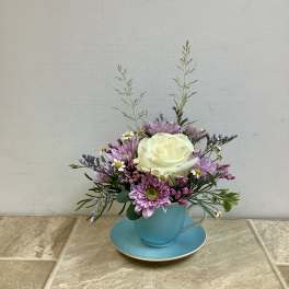 Small floral arrangement in a blue teacup and saucer with pink and white blooms