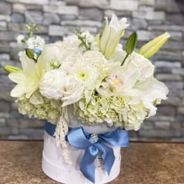 White floral arrangement in a round box with a blue ribbon