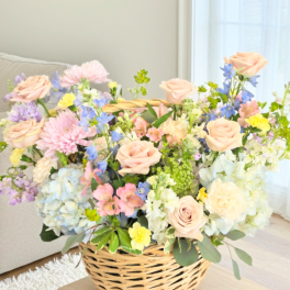 Basket arrangement of pastel roses, hydrangeas, and mixed blooms