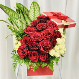 Red and white roses arranged in a gift box with a red ribbon and bow