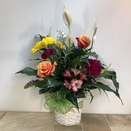 Mixed flower arrangement in a white basket with a green ribbon